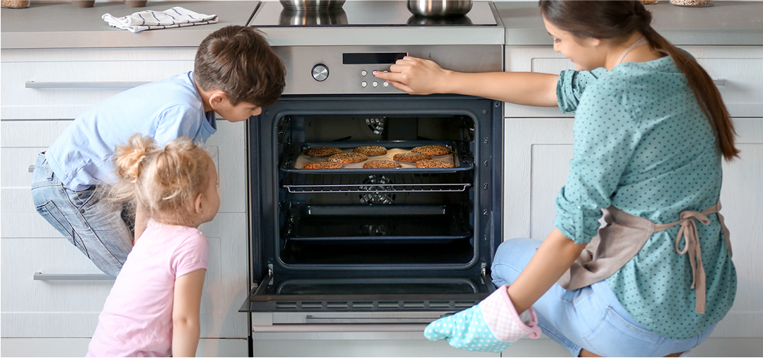 a woman and two children in the kitchen looking at food in the oven