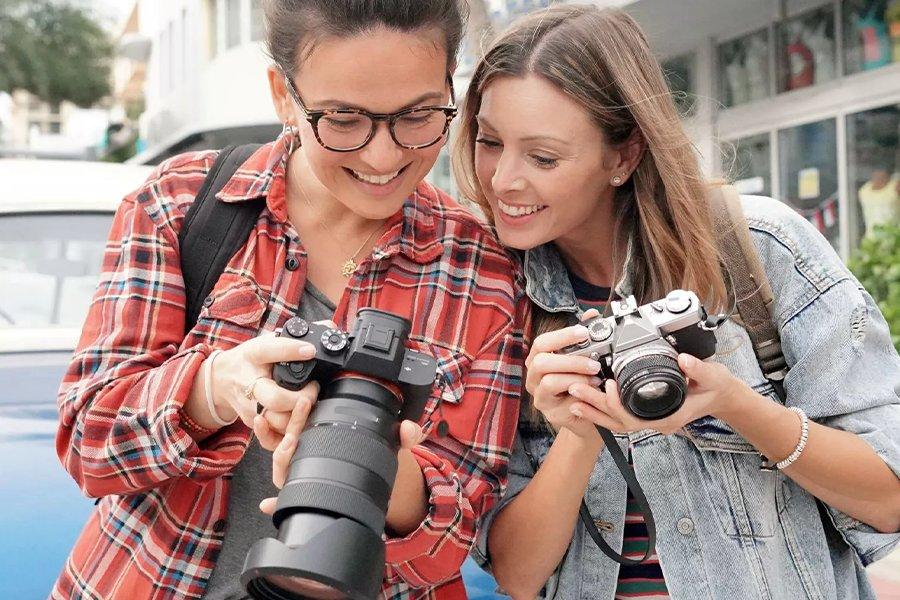 Two women are holding cameras and looking at the display on the back of one of them