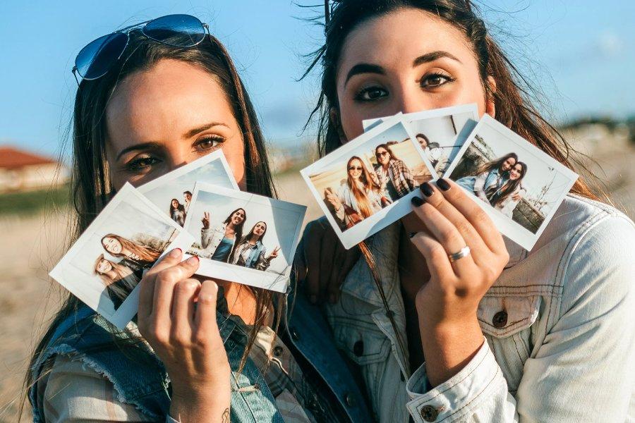 Two women holding three polaroid photos each, fanned out in front of their faces