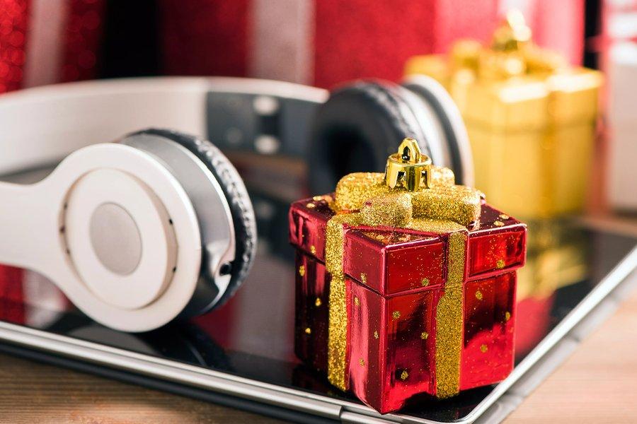 A pair of headphones and a small red gift box sit on top of a tablet