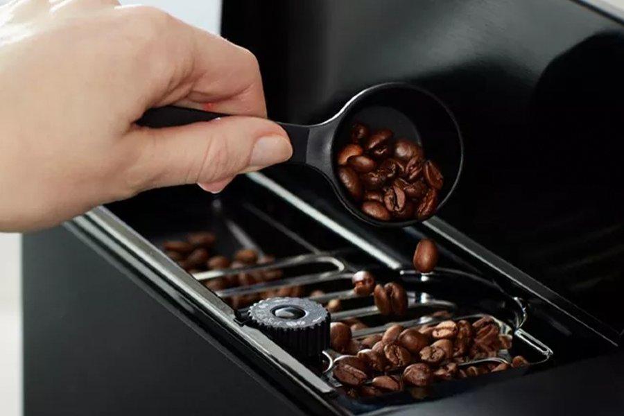 A hand pouring coffee beans into a coffee machine