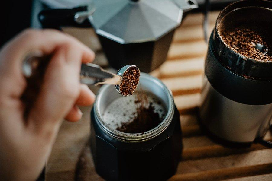A hand holding ground coffee in a scoop