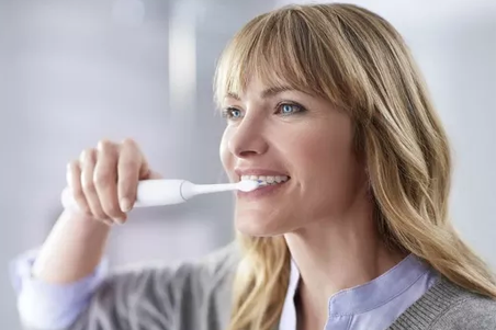 a woman brushing her teeth with an electric toothbrush