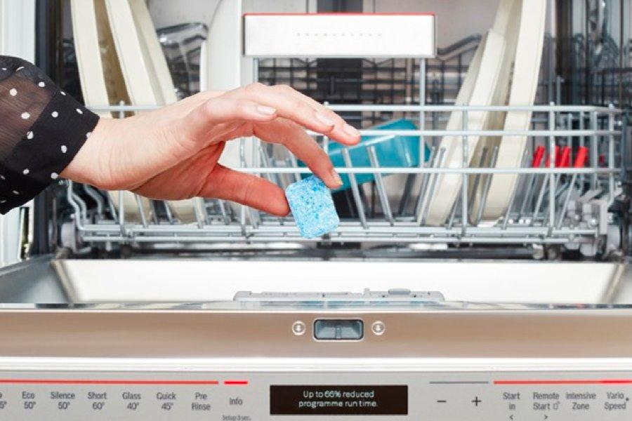 A hand putting a dishwasher tablet into a full dishwasher