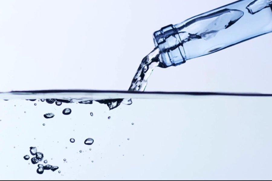 The neck of a glass bottle pouring a clear liquid into more liquid