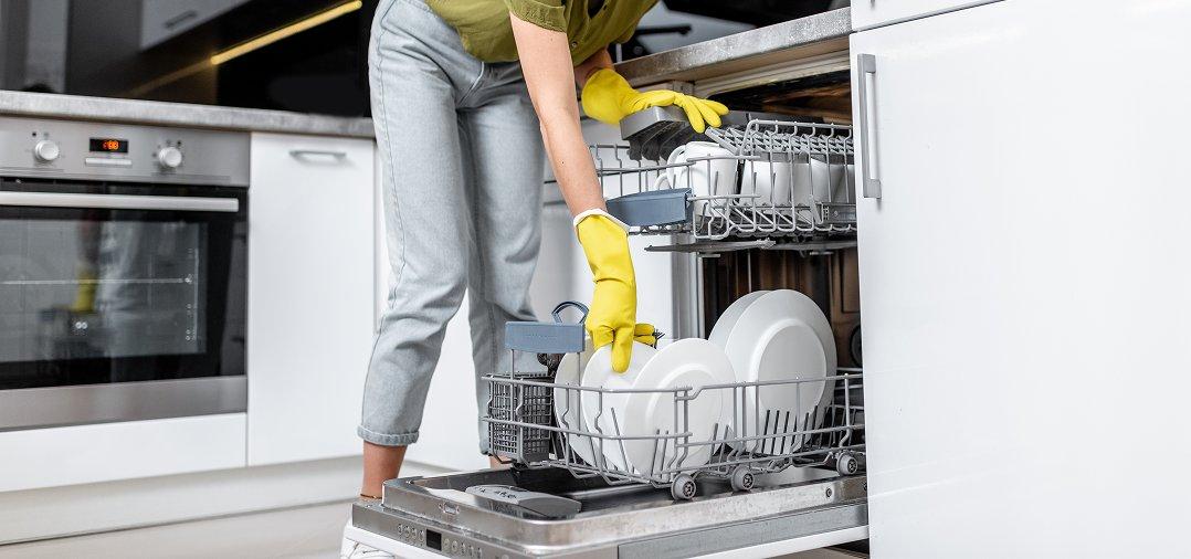 a woman in yellow gloves and yellow rubber gloves loading a dishwasher
