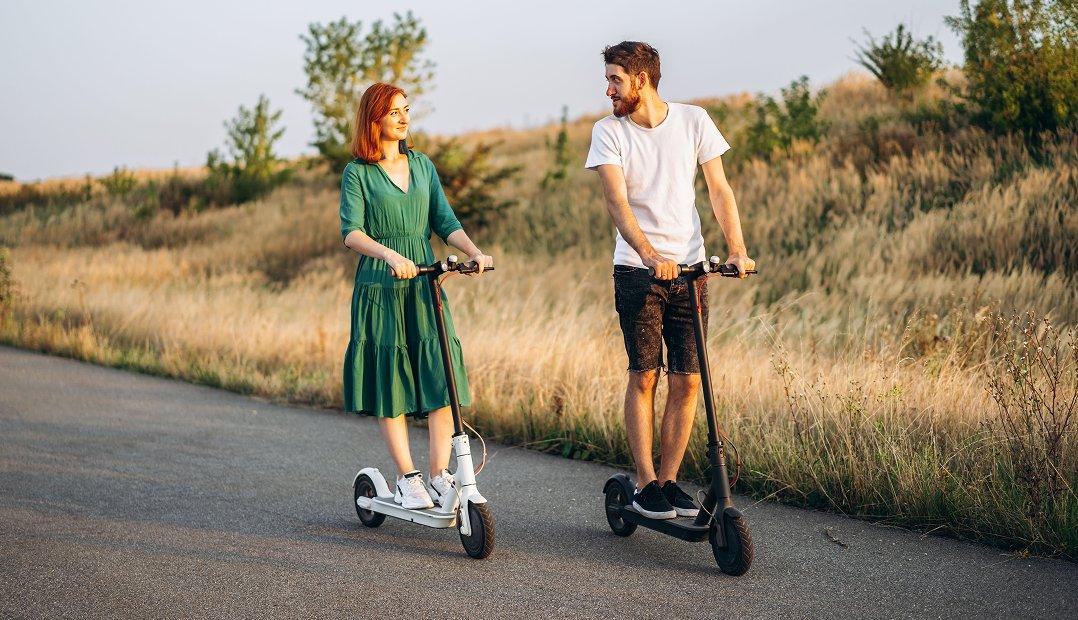a man and woman riding electric scooters on a road