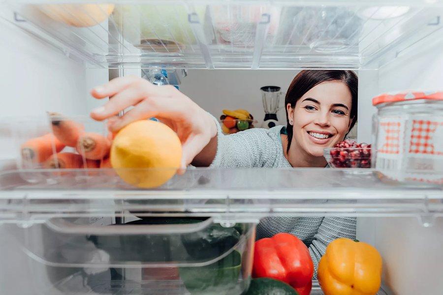 A woman opening fridge holding fruit