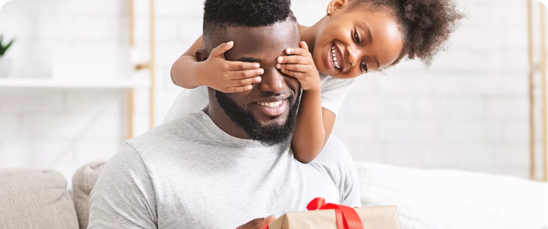 A child is covering their father's eyes whilst he holds a present