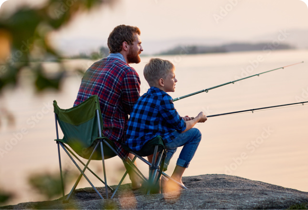 A father and son sitting beside a body of water whilst fishing