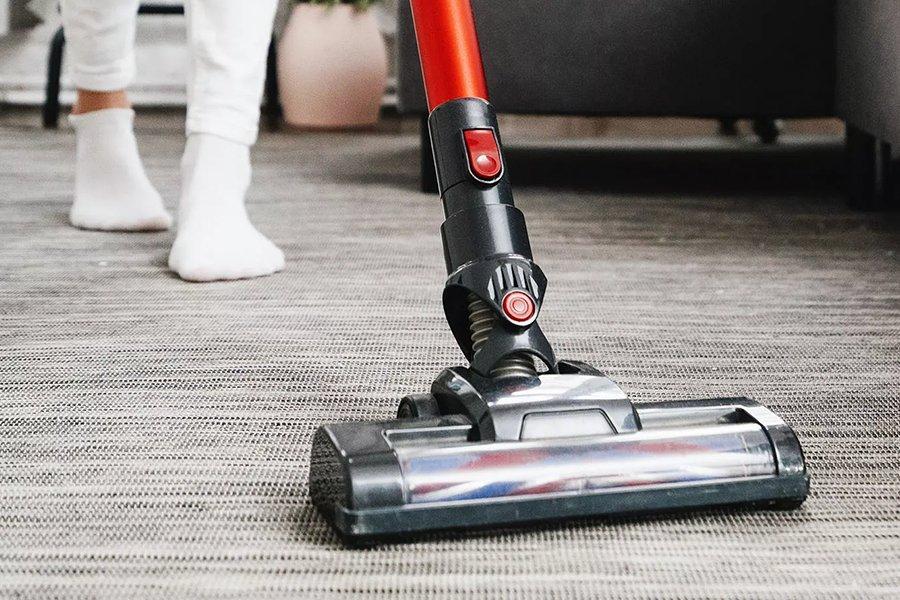 A vacuum cleaner on a carpet with a pair of feet behind