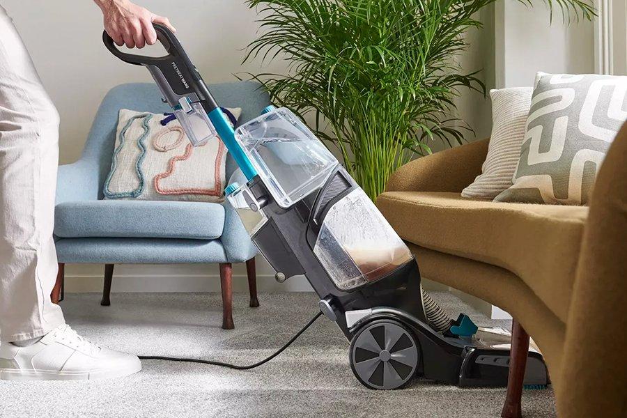 A carpet cleaner being pushed under a yellow sofa