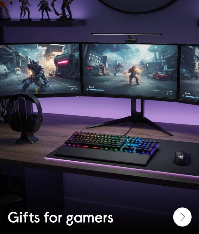 A gaming desk with three monitors and a backlit keyboard