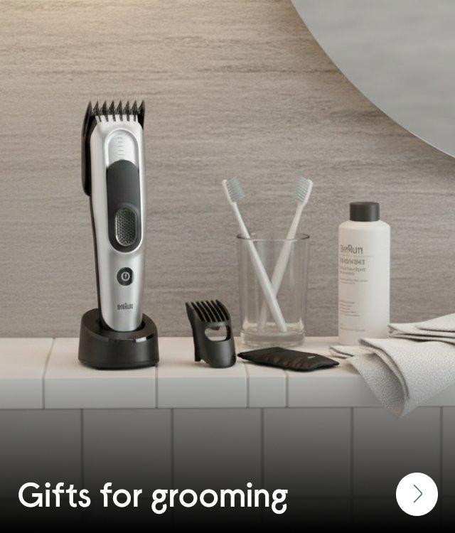 An electric shaver on a shelf in a bathroom next to toothbrushes and cream