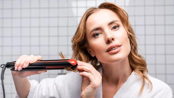 a woman in a white robe using hair straighteners