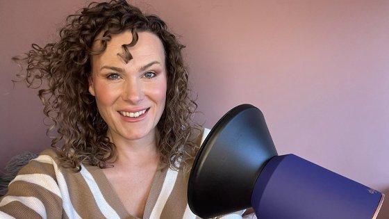 a woman with curly hair holding a blow dryer in her hand