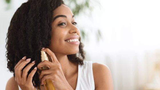 a woman is smiling while holding a bottle of hair oil