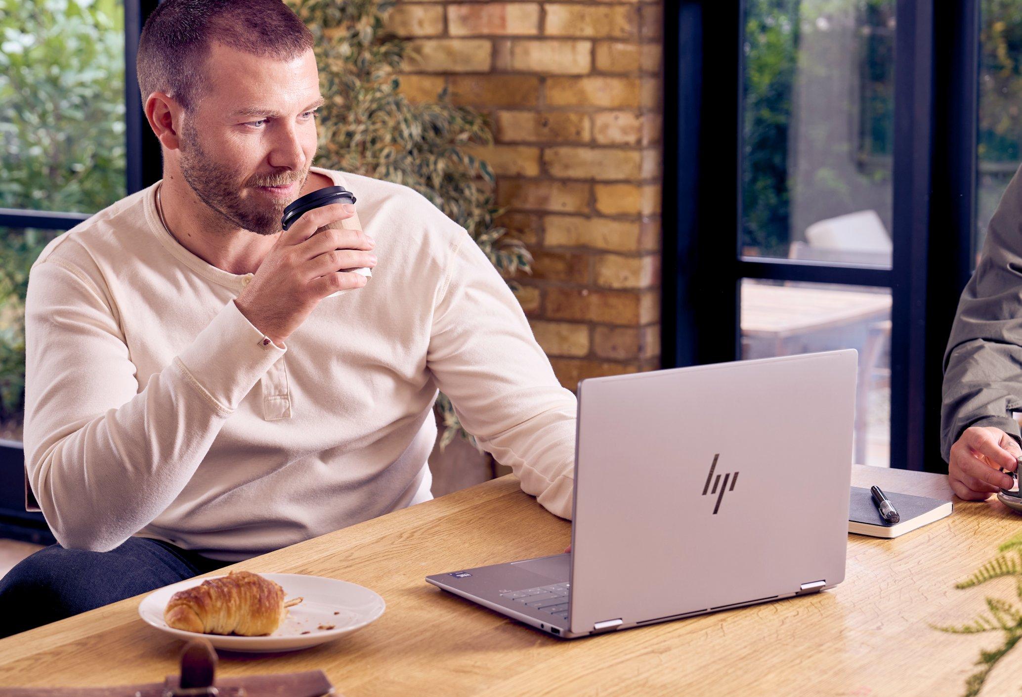 a man sitting at a table with a laptop and a cup of coffee