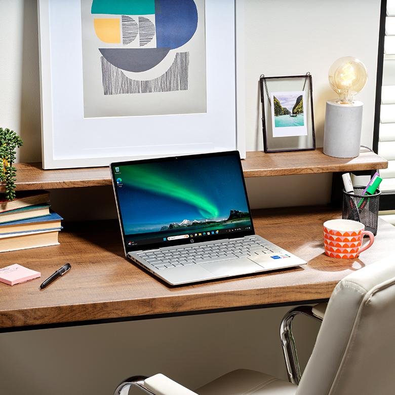 a laptop computer sitting on a desk next to a mug and a book