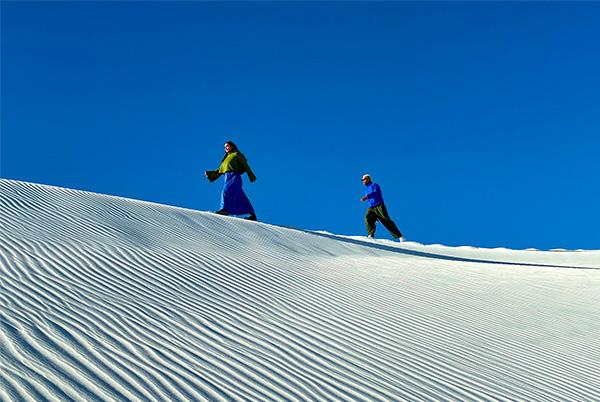 two people walking on a white sand dune in the blue sky