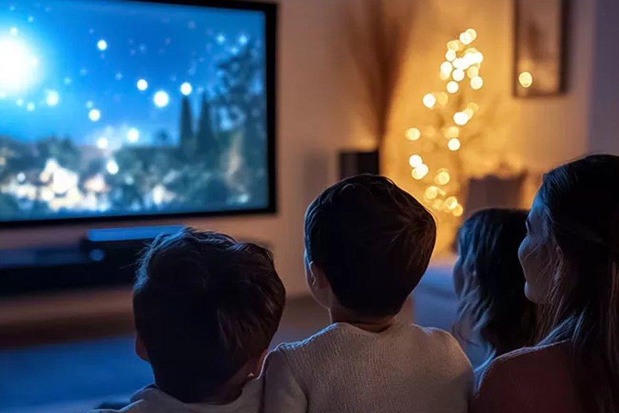 Four people sitting on a sofa watching a large TV