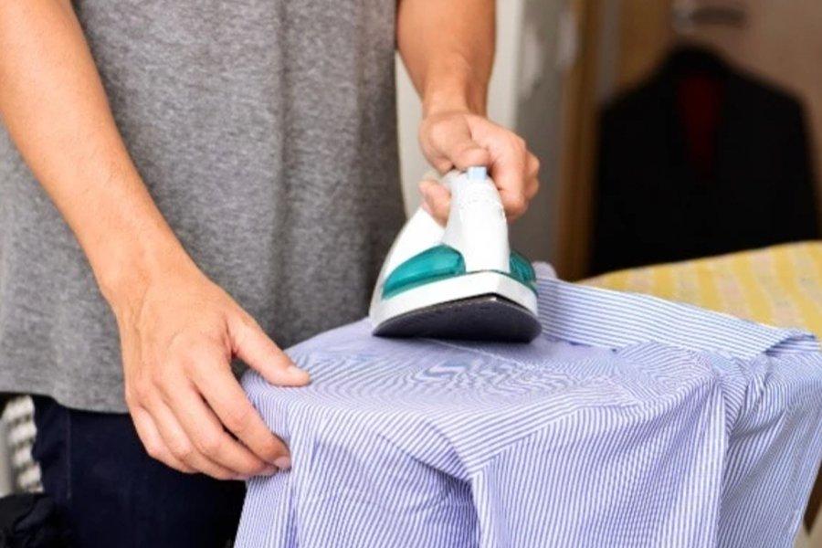 A person ironing a blue shirt on an ironing board