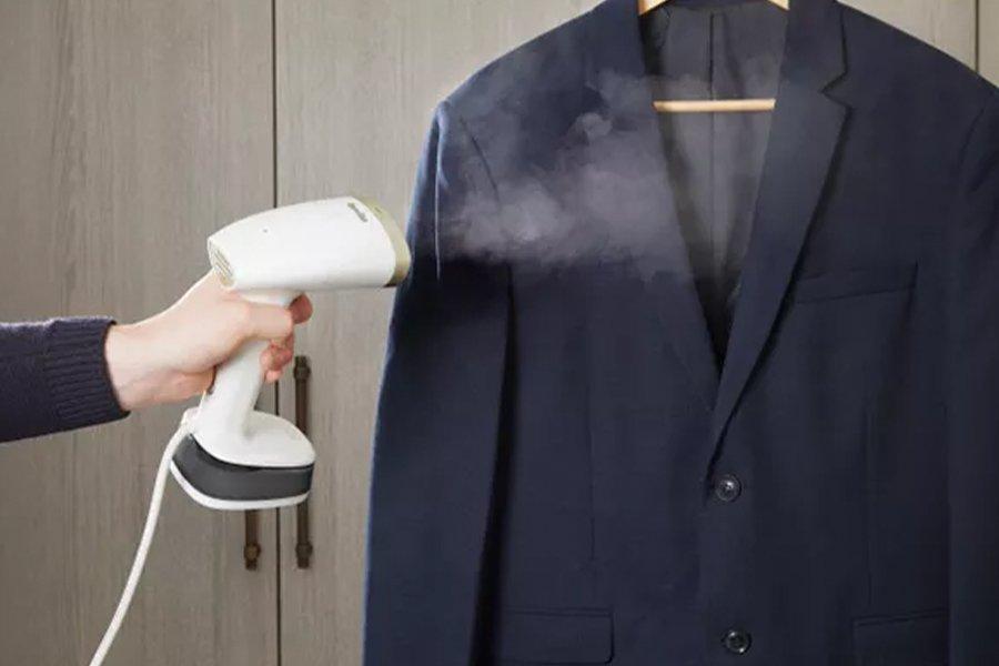 A hand holding a clothes steamer next to a black blazer