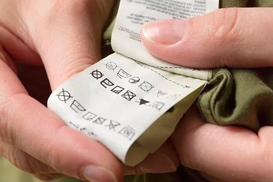 A close up of a person holding a washing label inside a piece of clothing