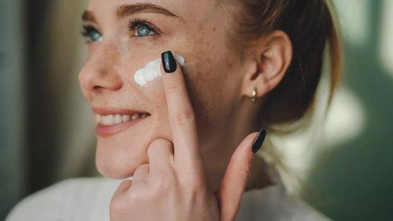 a woman with black nail polish is applying cream to her face