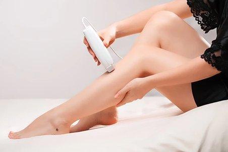 a woman sitting on a bed with an IPL hair removal device on her leg