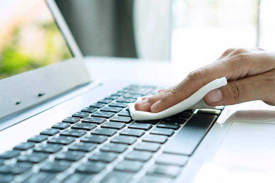 A hand using a cloth to wipe a laptop keyboard