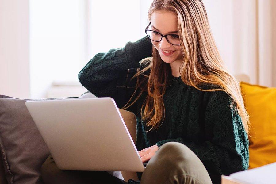 A smiling woman sitting on a sofa looking at a laptop