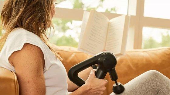 a woman sitting on a couch reading a book with a massage gun