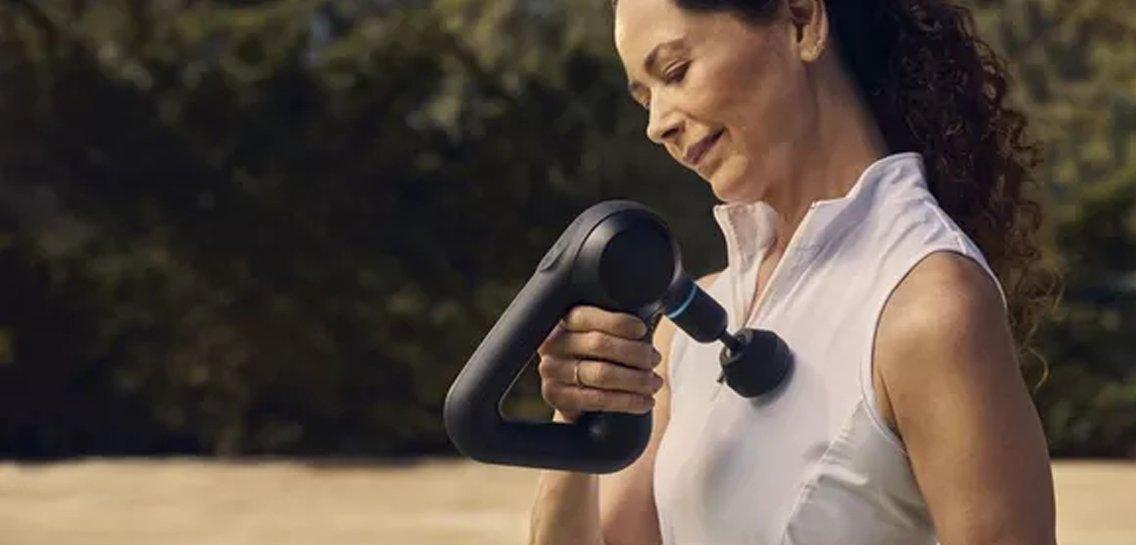 a woman holding a black massage gun in her hand while standing in the grass