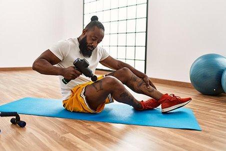 a man is working out on a mat with a massage gun