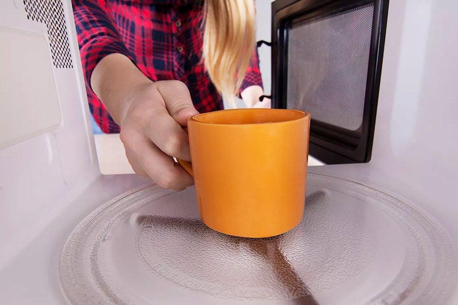 A person putting an orange mug into a microwave