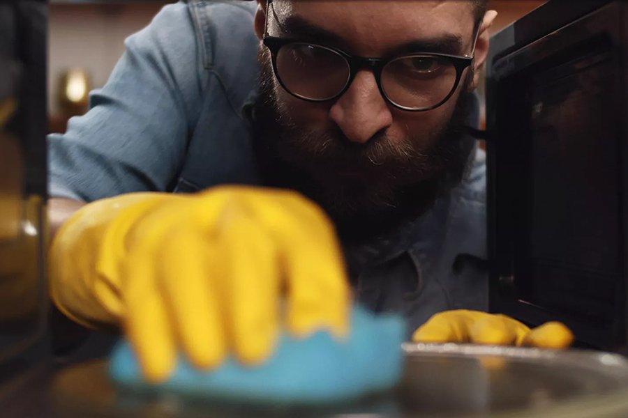 A man wearing a yellow glove cleaning the inside of a microwave