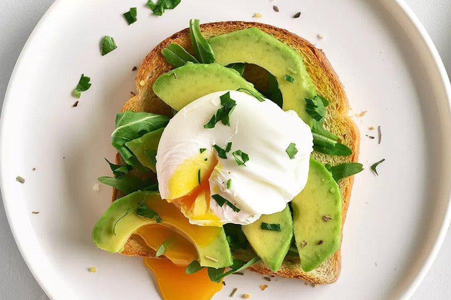 A plate with toast, avocado and a poached egg layered on top