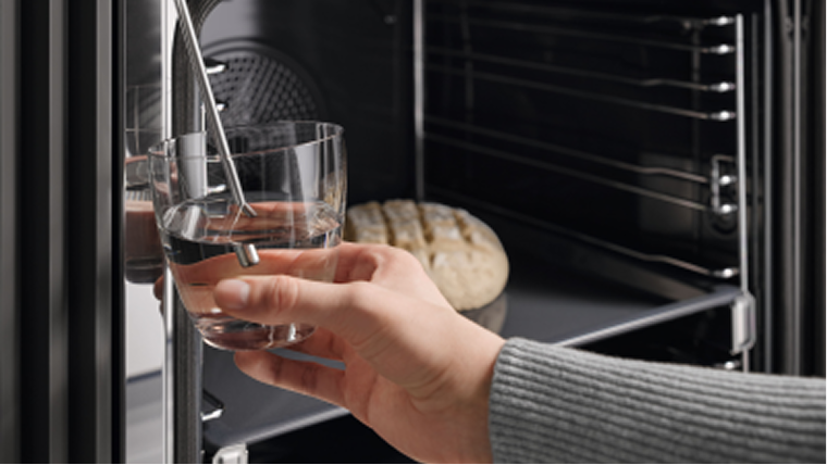 A hand holding a cup of water up to an open built-in oven