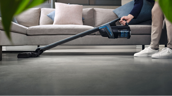 A person holding a cordless vacuum cleaner stretched over a floor