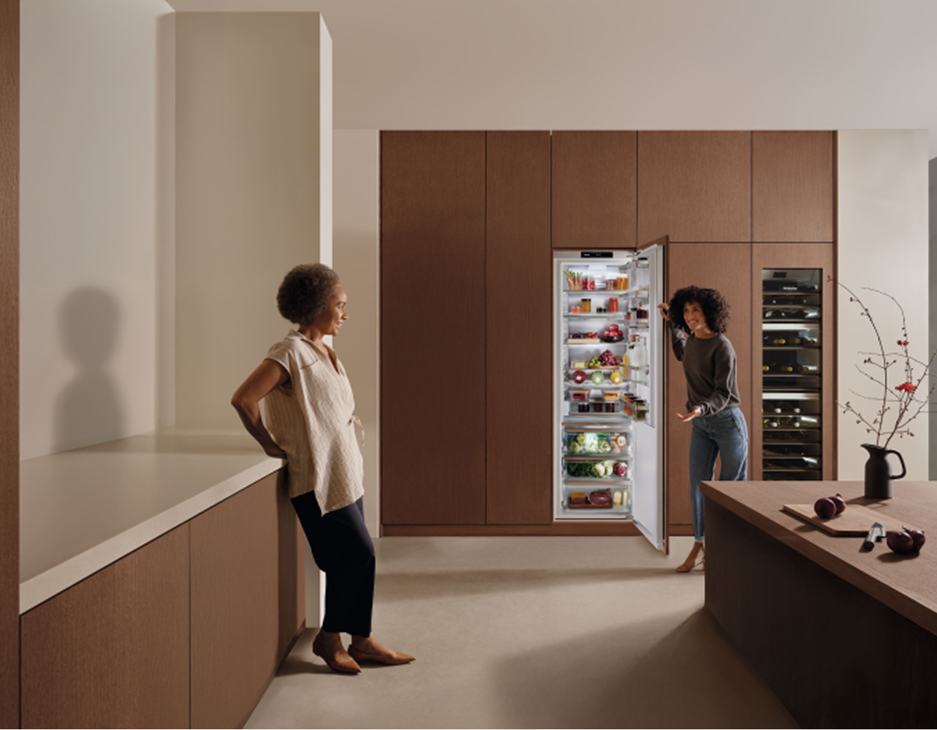 Two women are in a kitchen, one is opening a built-in fridge