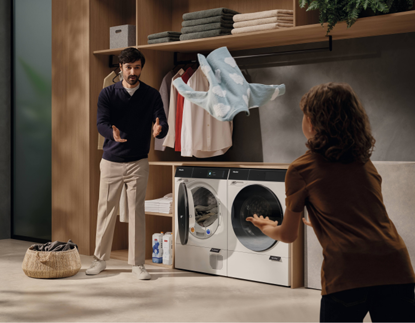 A man is throwing a top to a woman whilst they stand in a laundry room