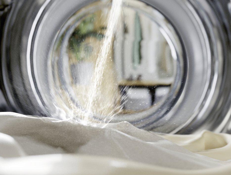 A washer dryer drum with clothes in it and a stream of water