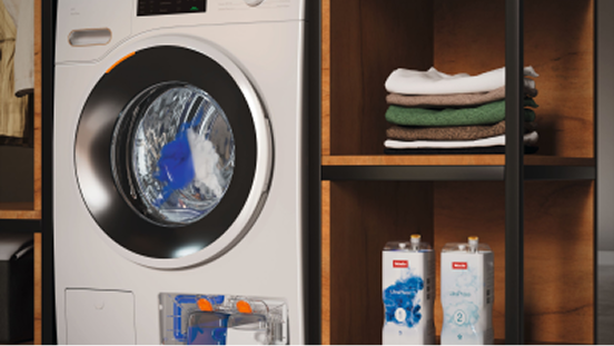 A washing machine in a shelving unit next to detergent and a stack of clothes
