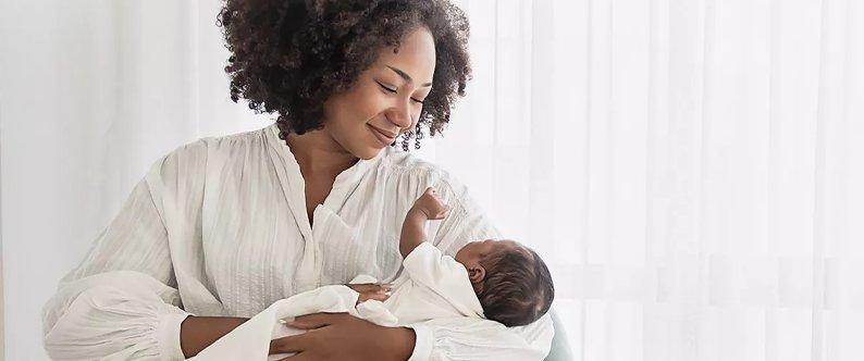 A mother holds a newborn baby whilst smiling