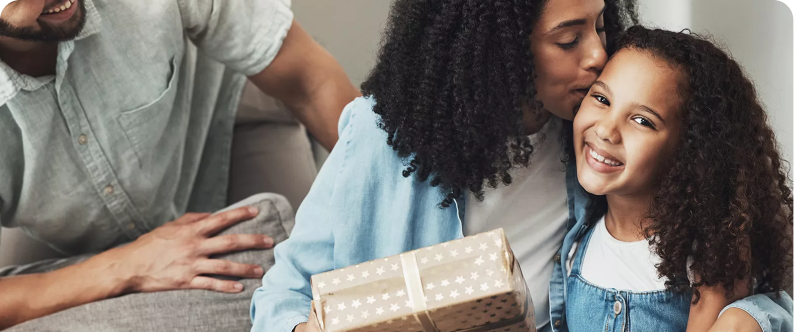A woman kisses a young girl on the forehead whilst holding a gift