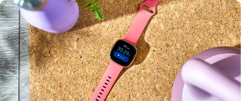 A smart watch with a pink strap lying on a cork-style surface