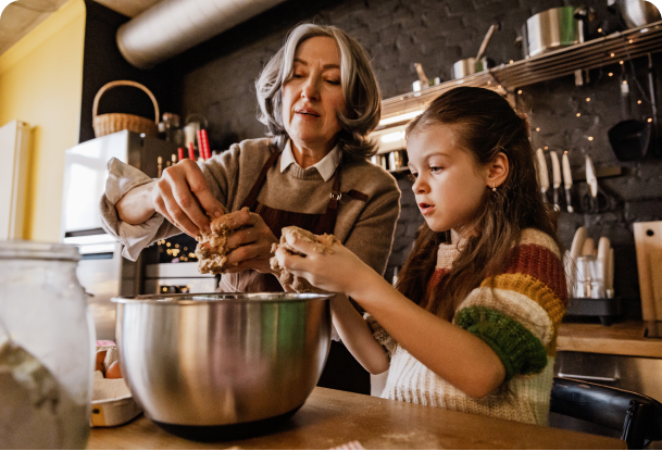 An older woman and young girl putting ingredients into a bowl in a kitchen