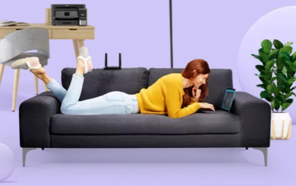 A woman lying on a sofa using a laptop