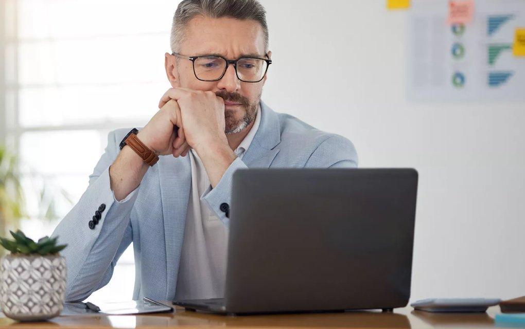 A man sitting at a table looking at a laptop